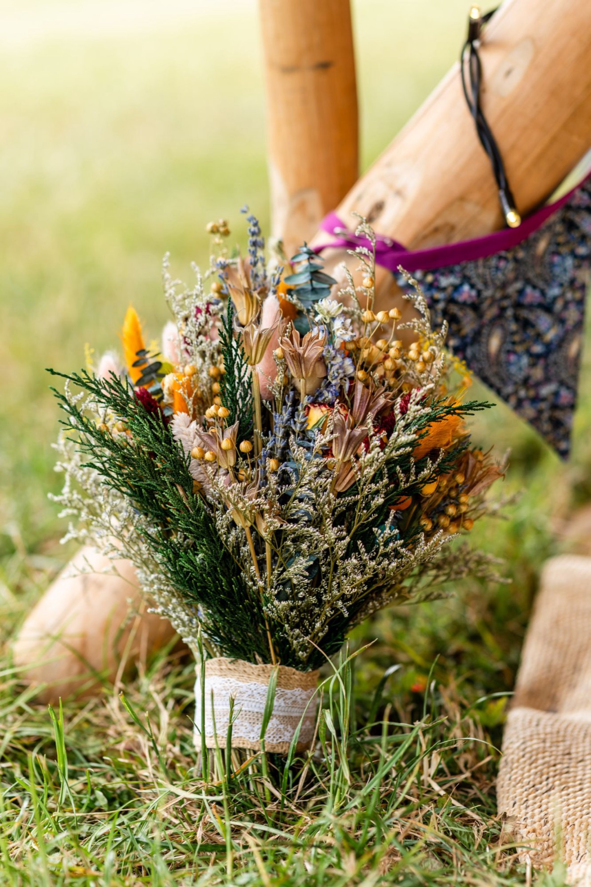A wildflower wedding bouquet wrapped in hessian and lace, resting on the grass