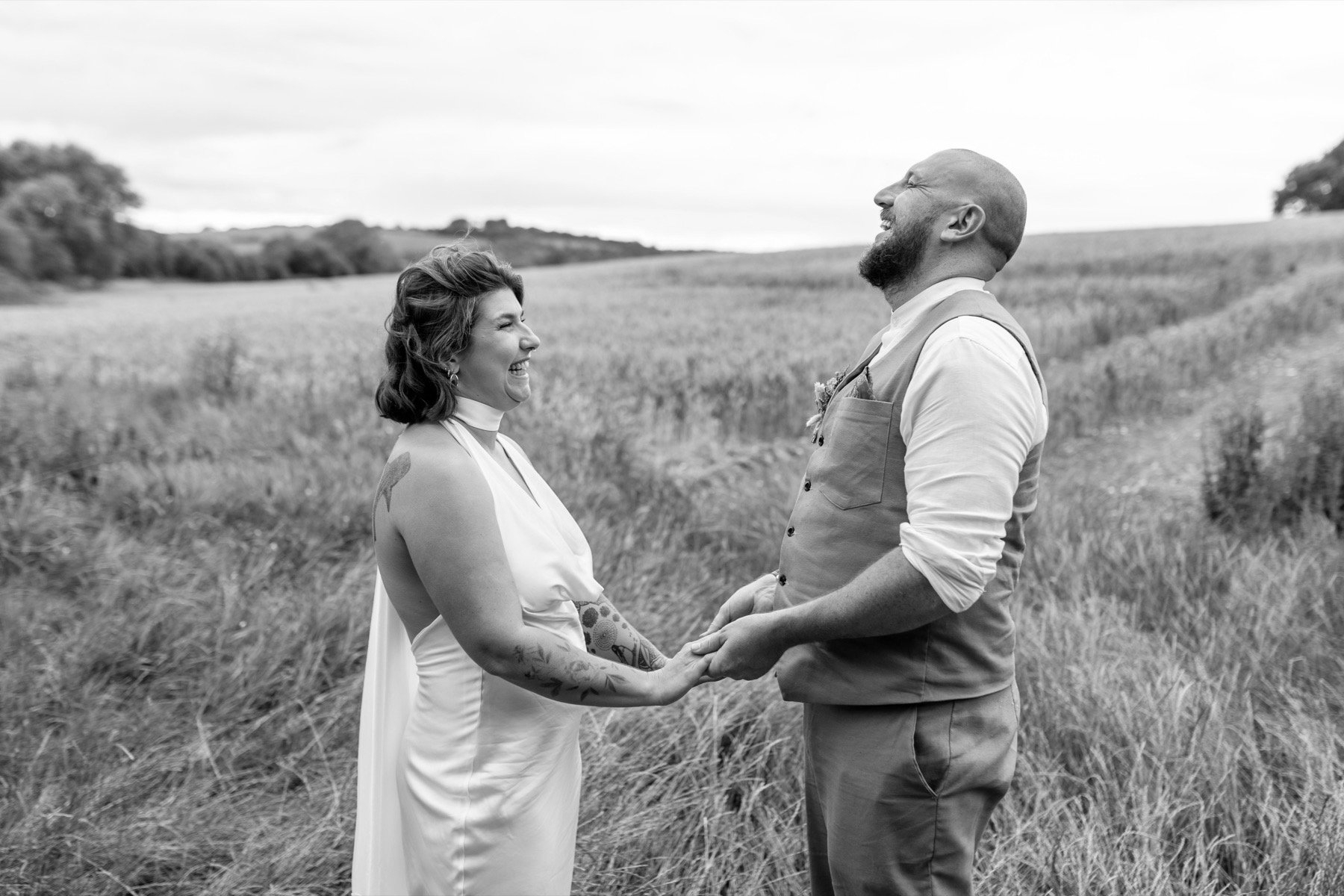 The newly married couple laughing together, holding hands in a field